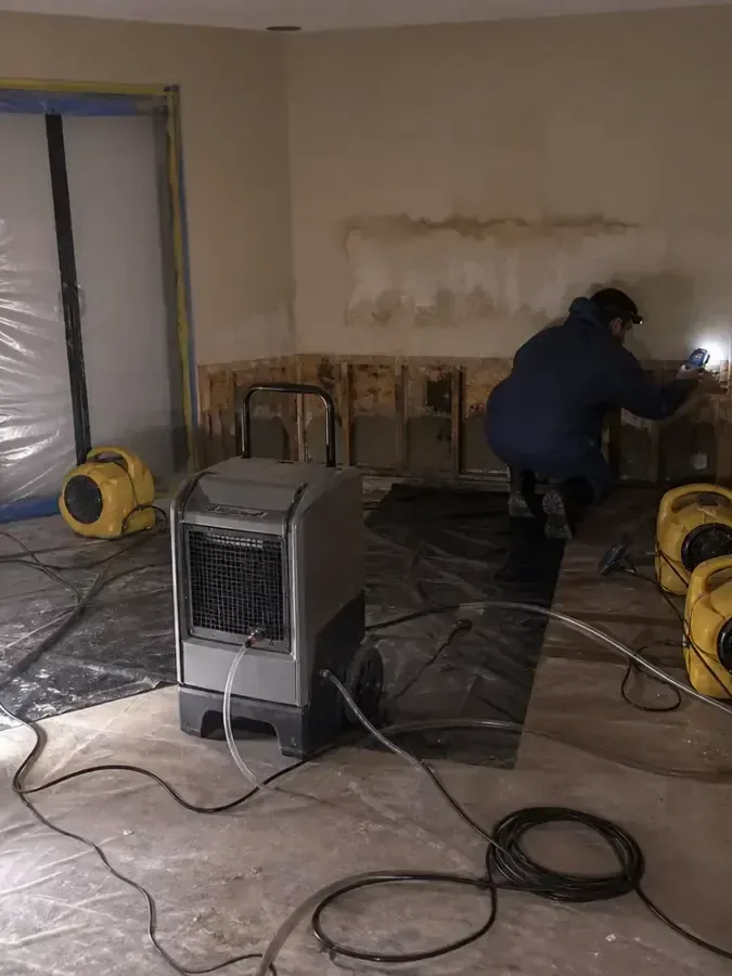 A technician works beside drying equipment in a room with opened wall bottoms