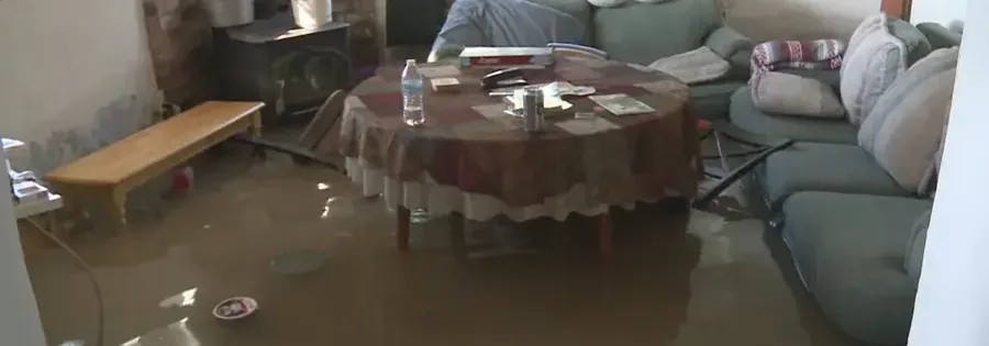 Floodwater stands across a furnished living room floor around chairs and a table