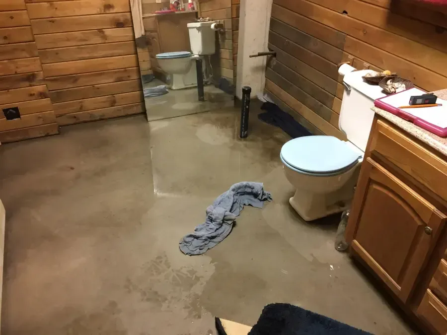 Water spreads across a bathroom floor beside a toilet and vanity